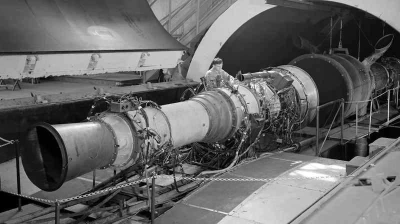 Black and white photo of a long jet engine mounted in a wind tunnel test section