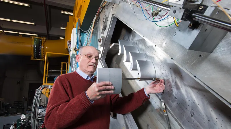 An engineer holds a turbine blade beside a test rig lined with blade shapes