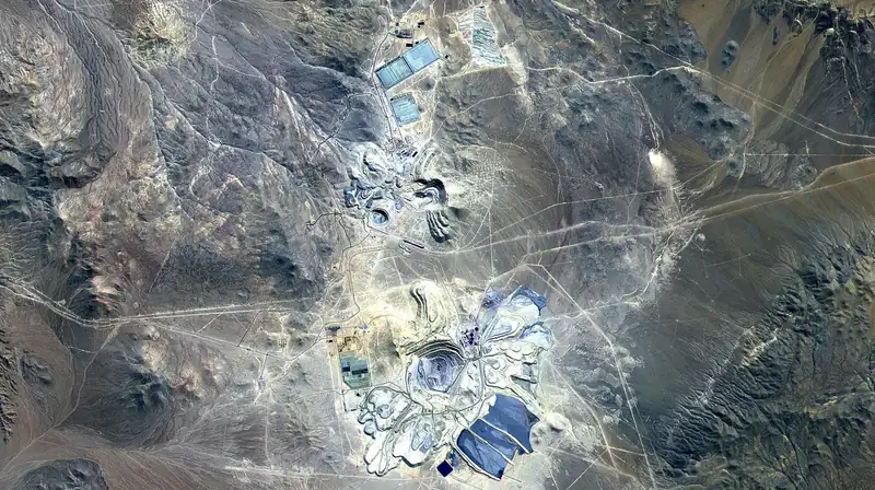 Satellite image of the Escondida copper mine: grey pits and pale leach pads in brown desert hills