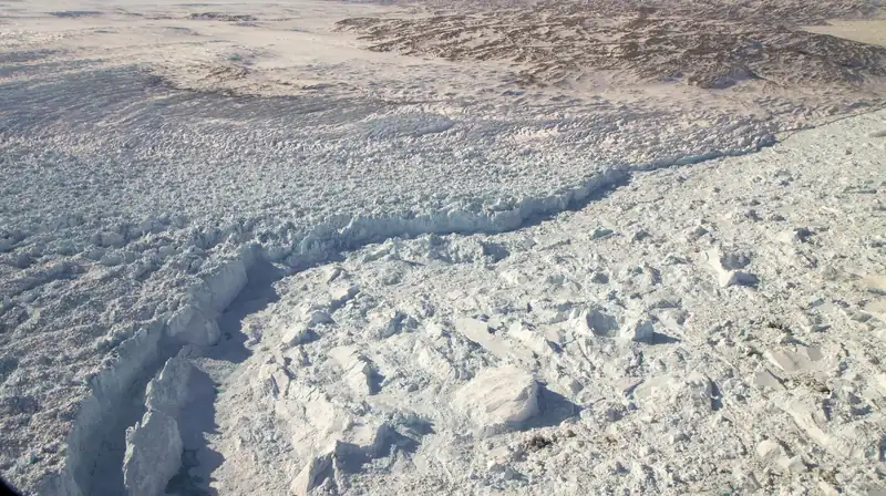 A wall of white glacier ice breaking into a fjord crowded with icebergs