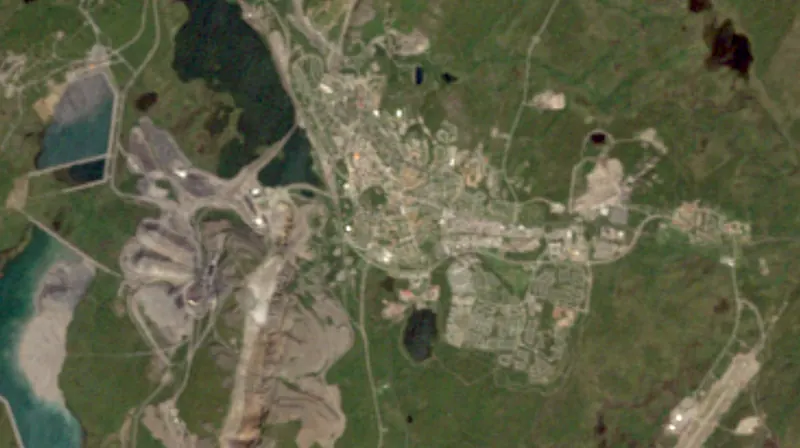 True-colour satellite image of Kiruna, about 11 km across: the mine and its plant on the left, the caved ground over the ore, the old town on its hill in the middle and the new centre to the east
