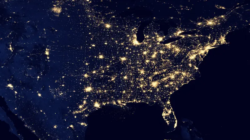 The United States at night seen from space, cities glowing gold along a dark blue land