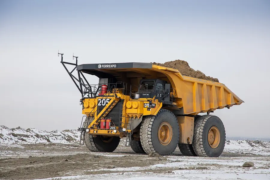 A yellow haul truck loaded with ore, with a rack of sensors on its front and an empty cab, on a snowy mine road
