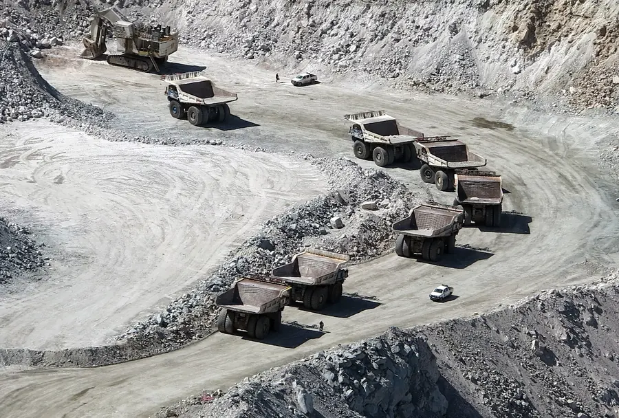 A line of haul trucks driving up a curving ramp out of a pale open pit