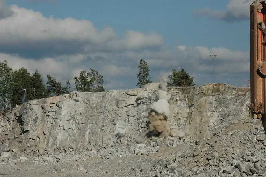 A quarry rock face before a blast, intact, and a moment after, swollen and slumped forward into broken rock