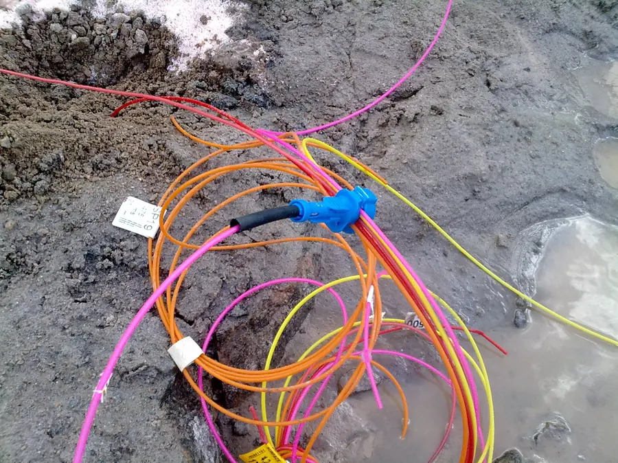 Orange, pink and yellow shock tube lines joined by blue connectors, lying on rock and snow