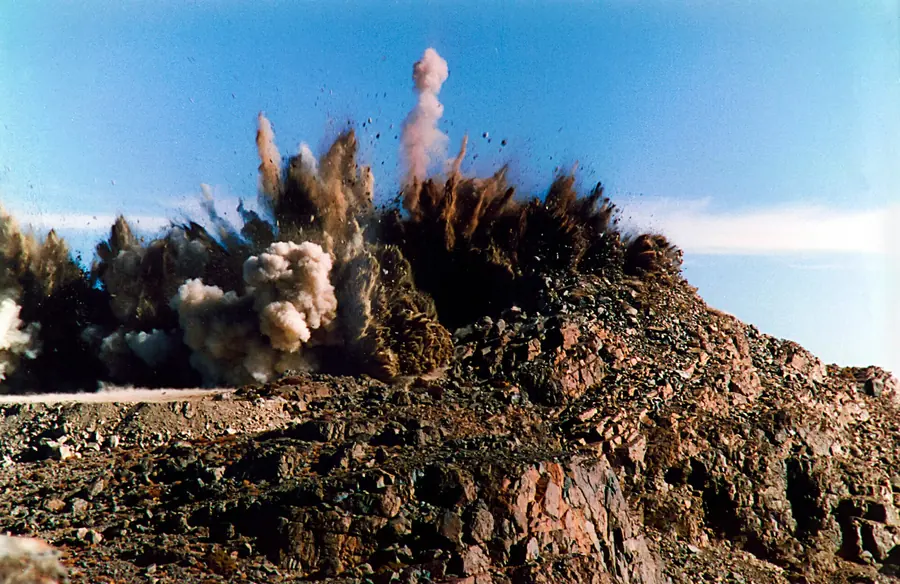 A blast throwing dark rock and dust into a blue sky on a rocky hilltop