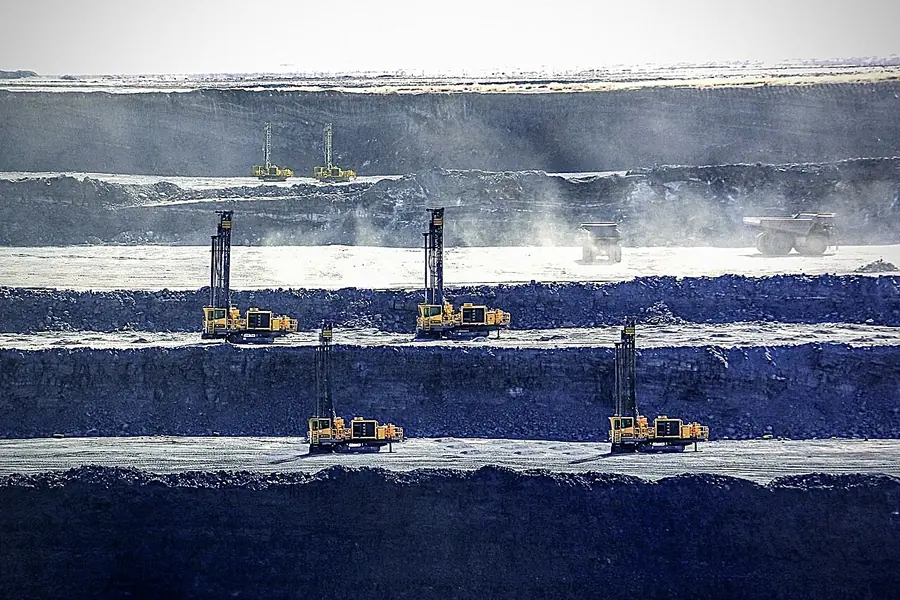Five tall drill rigs spread across the dark benches of an open pit, drilling blastholes