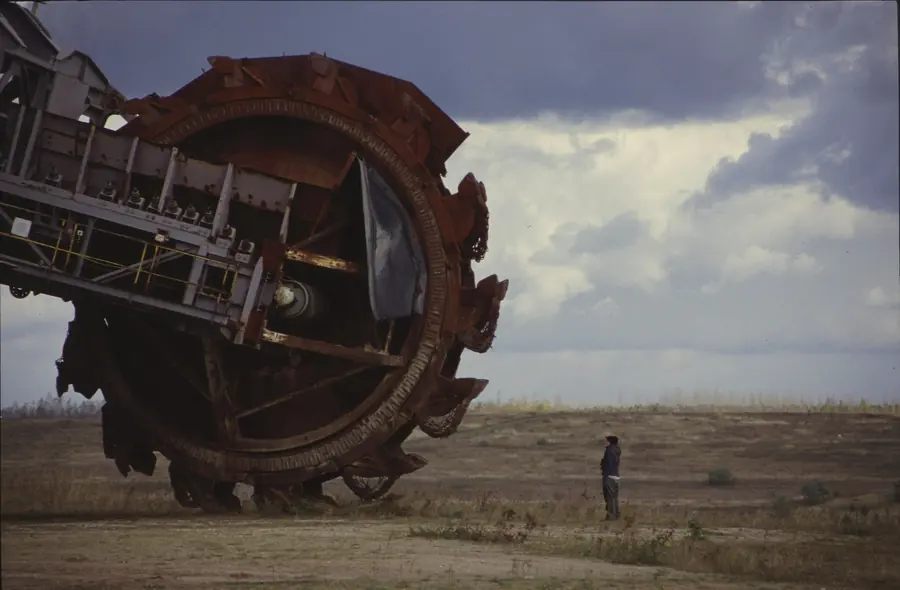 A rusted bucket wheel on its boom, many times the height of the person standing beside it