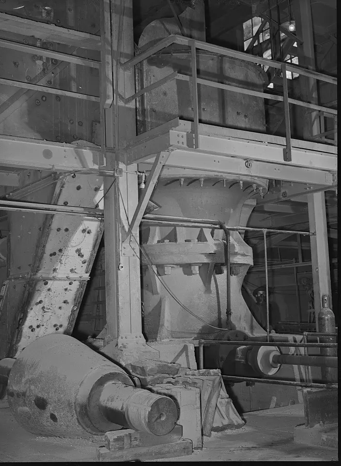 A tall gyratory crusher in a steel framed crusher house, with its drive shaft and motor at the base