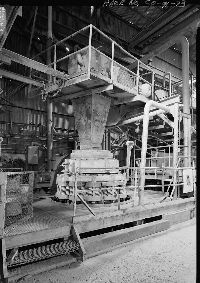 A Symons cone crusher under its feed conveyor and platform in a mill crushing room