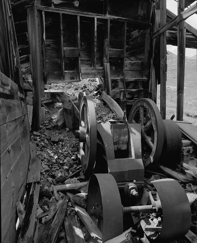 An old jaw crusher with two large flywheels in the ruined timber crushing floor of a mountain mill