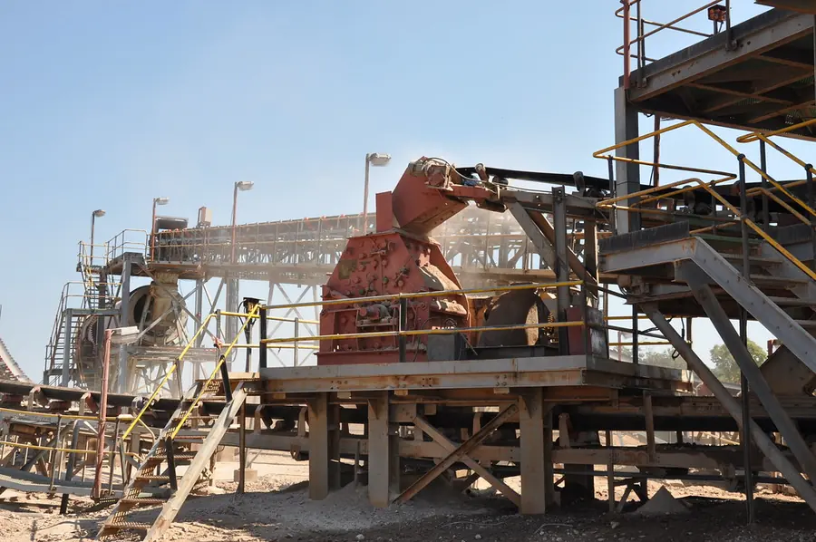 A large red crusher inside the steel frame of a crushing plant, with conveyors and walkways around it