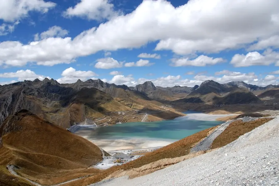 A pale turquoise tailings pond filling a high Andean valley below rugged peaks