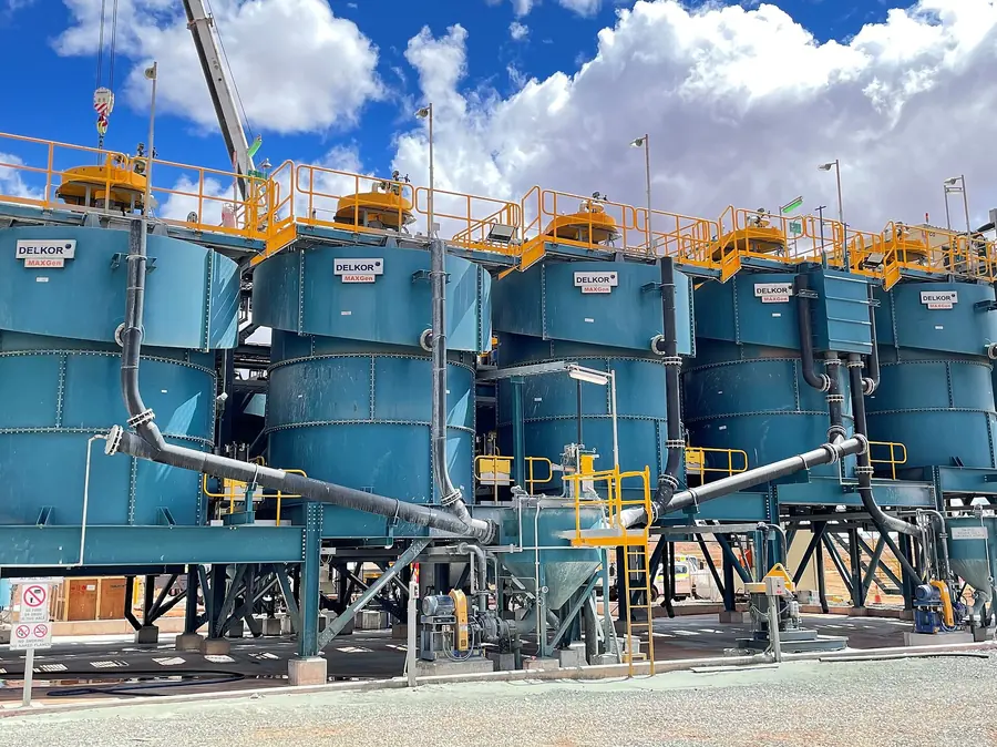 A row of tall blue flotation tank cells with walkways and pipes under a blue sky