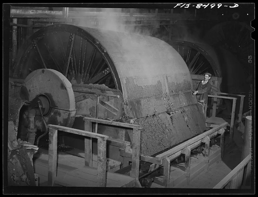A large drum filter with a worker standing beside it in a steamy plant