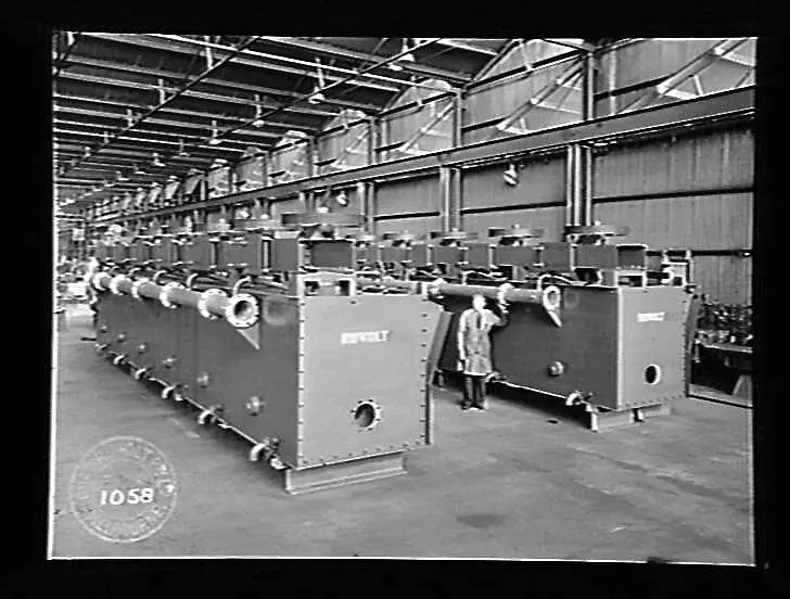 A long bank of new steel flotation cells in a workshop, with a man standing beside them