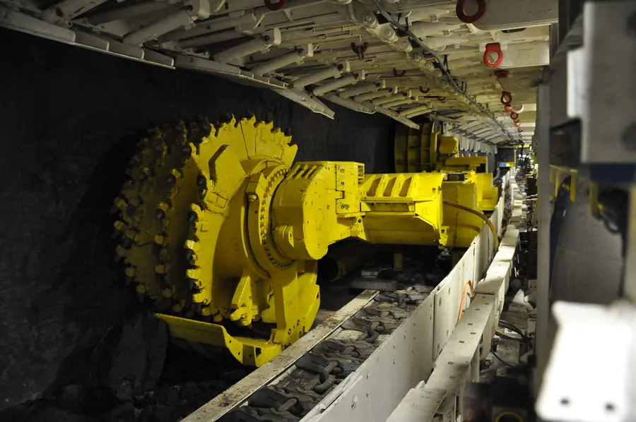 The yellow cutting drum of a longwall shearer under the steel canopies of the shields