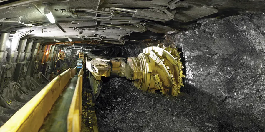 A shearer cutting coal beside a yellow armoured face conveyor under a row of shields