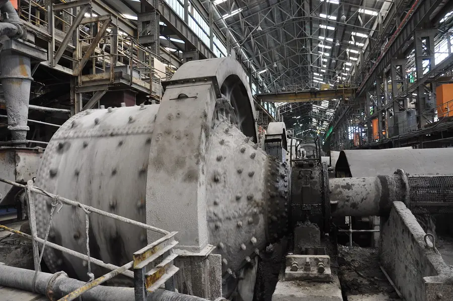 A large grey ball mill studded with liner bolts in a long mill hall