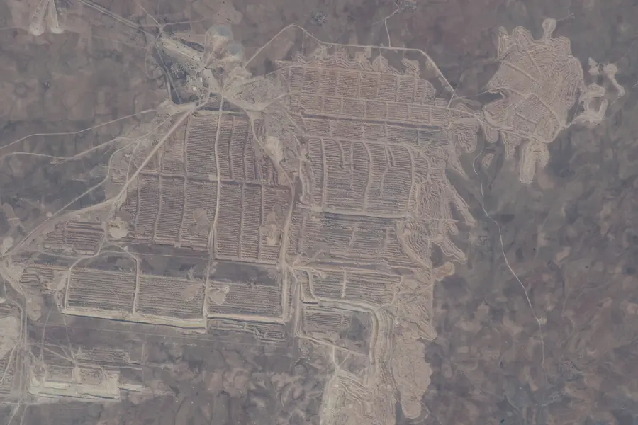 The pale terraced cuts of a huge open phosphate mine in desert, seen from orbit