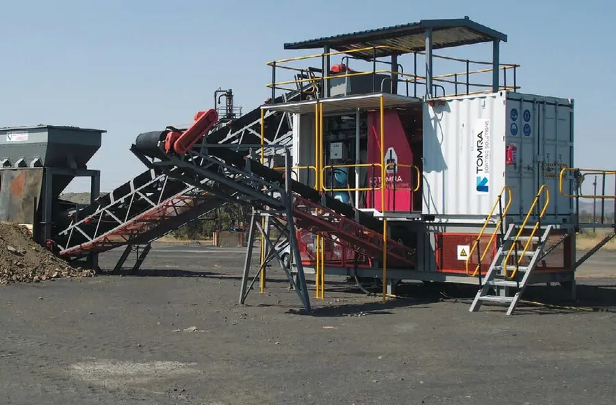 A containerised ore sorter on legs, fed by an inclined conveyor, at a mine site