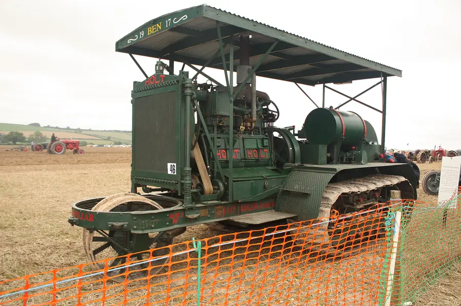 A green Holt 75 crawler tractor with a canopy roof and a steering wheel out front