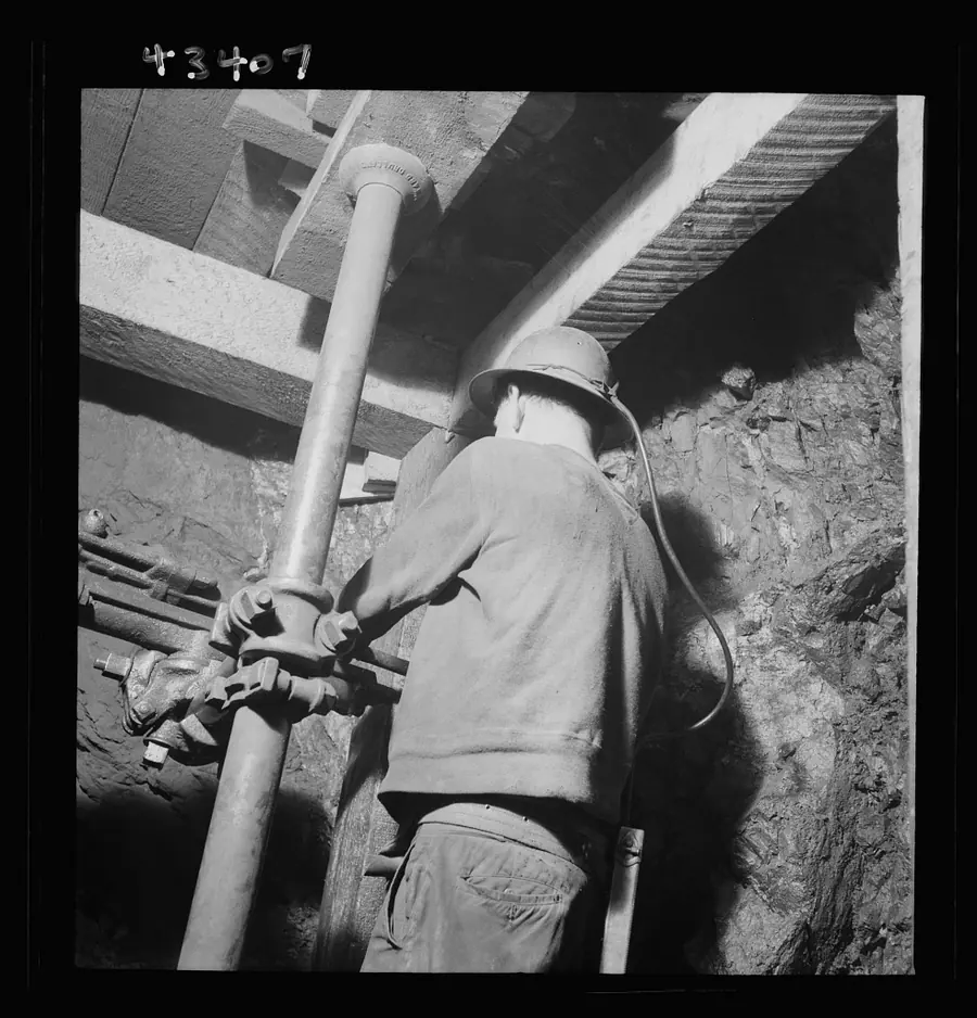 A miner in a hard hat braces a compressed-air rock drill against the rock overhead