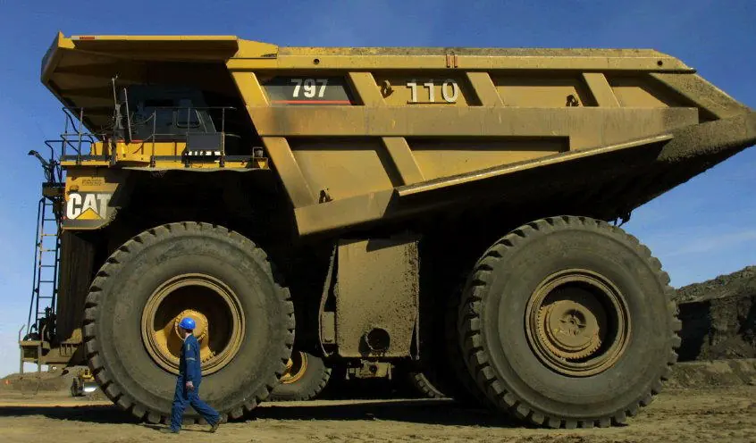 A Caterpillar 797 haul truck with a worker standing beside a front tyre that is more than twice his height