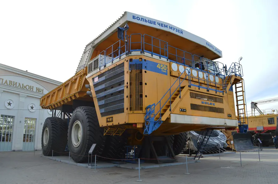 A yellow BelAZ 75710 dump truck on display, its cab platform level with the first floor of the building behind