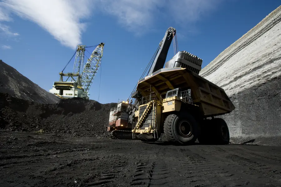 A haul truck being loaded with coal by an electric shovel, with a dragline working behind
