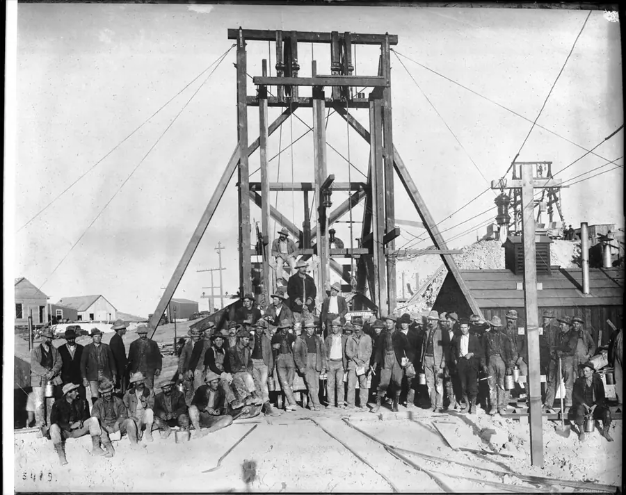 A shift of miners lined up in front of a timber headframe