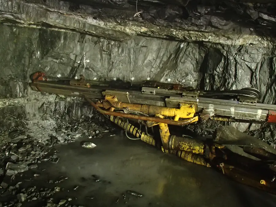 A yellow drill jumbo with its booms against the rock face of a tunnel
