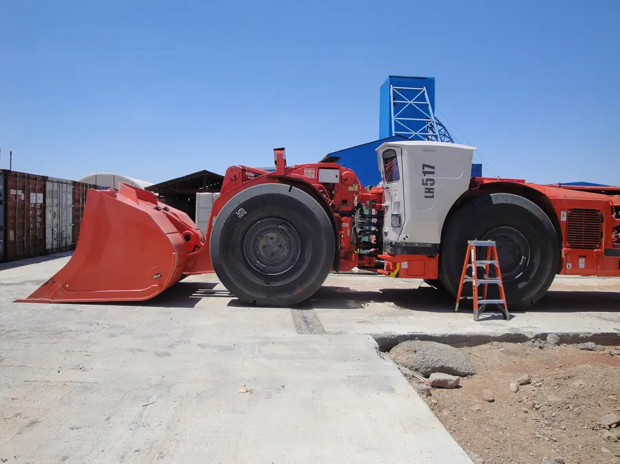 A big red and white underground loader with a red bucket, a ladder beside it