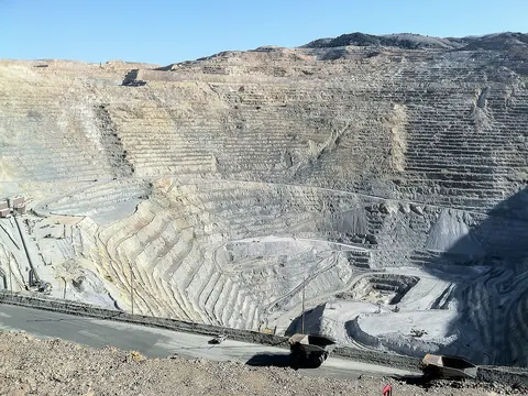 A vast terraced open pit with two haul trucks in the foreground