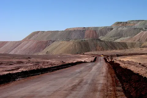 A dirt haul road leading toward terraced waste dumps under a blue sky