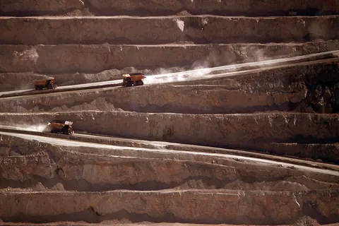 Three haul trucks on dusty ramps inside a desert open pit