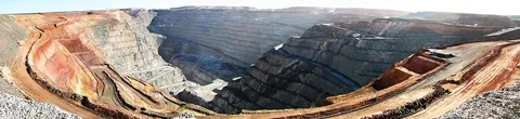 Panorama of a huge open pit with terraced red and grey walls